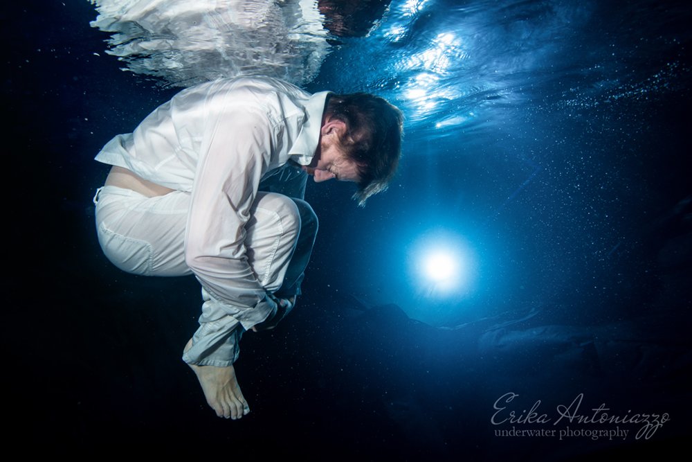 Onderwaterfoto model, man in witte broek en bloes, met licht in de verte, zwevend als in het universum