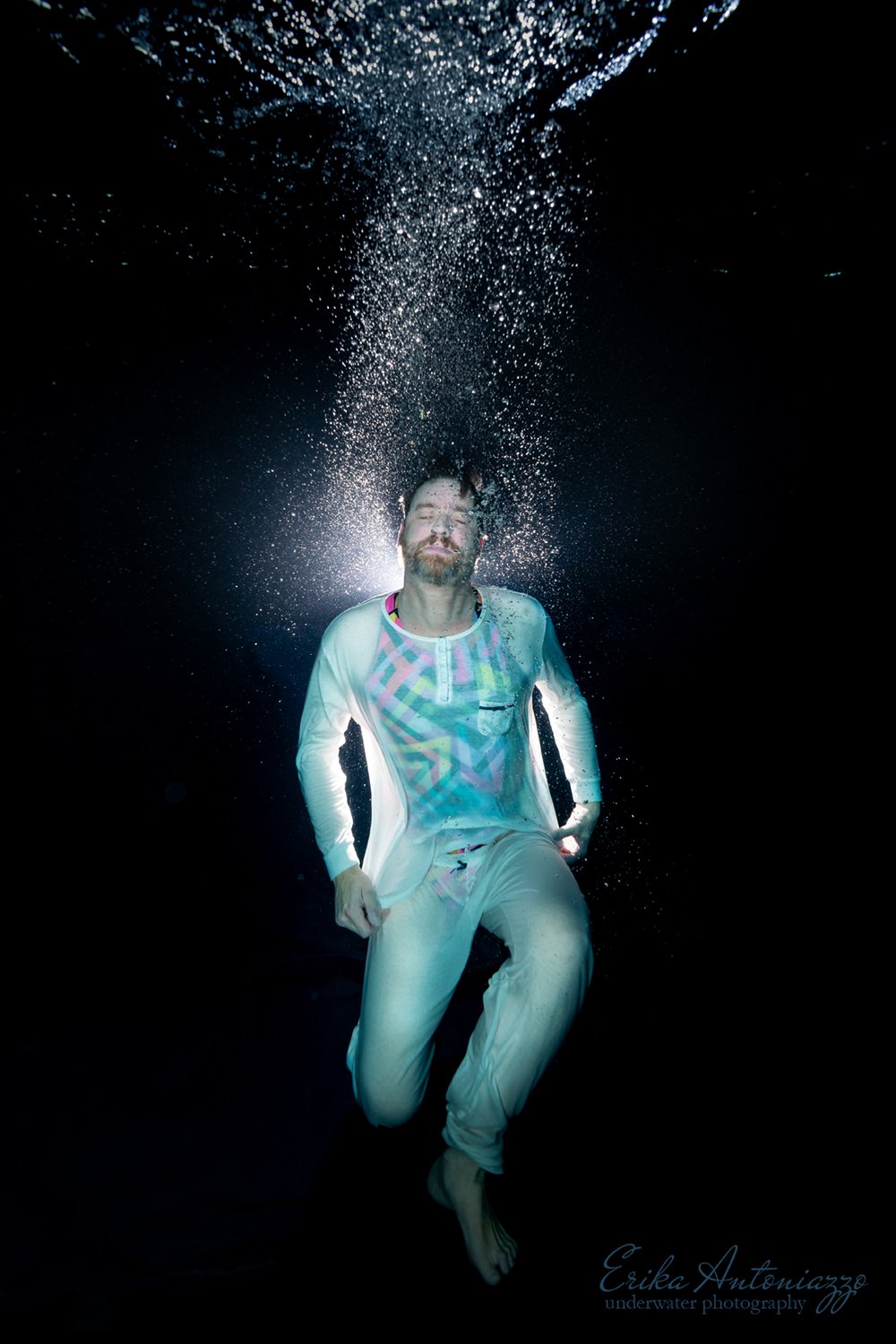 Onderwaterfoto model man in witte kleding met belichting van achteren en waterbellen