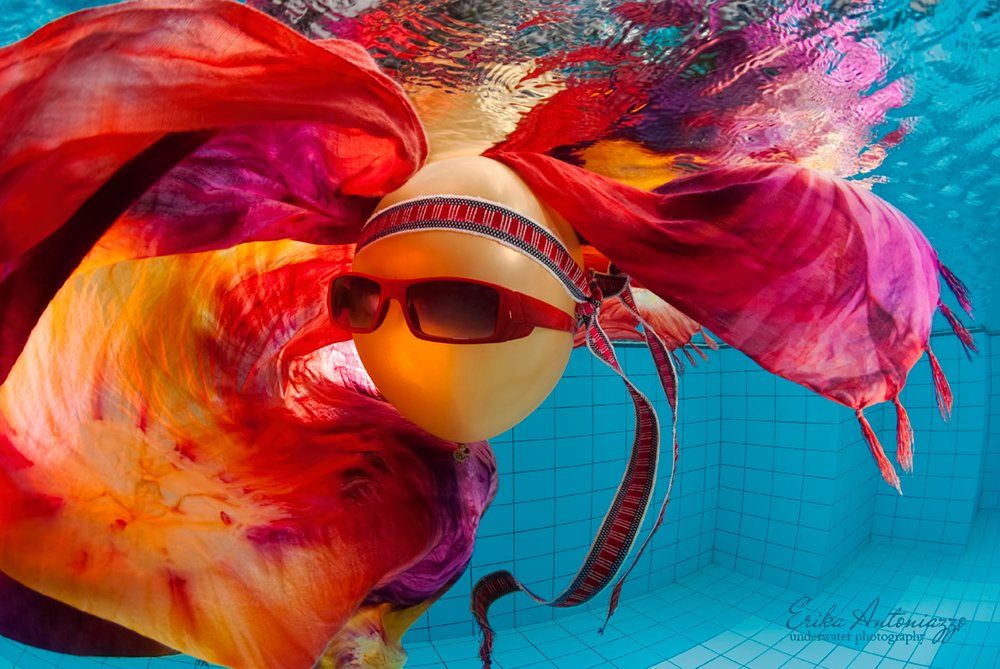 Goudkleurige ballon met zonnebril, bandanna en oranje-rode doek onder water in het zwembad