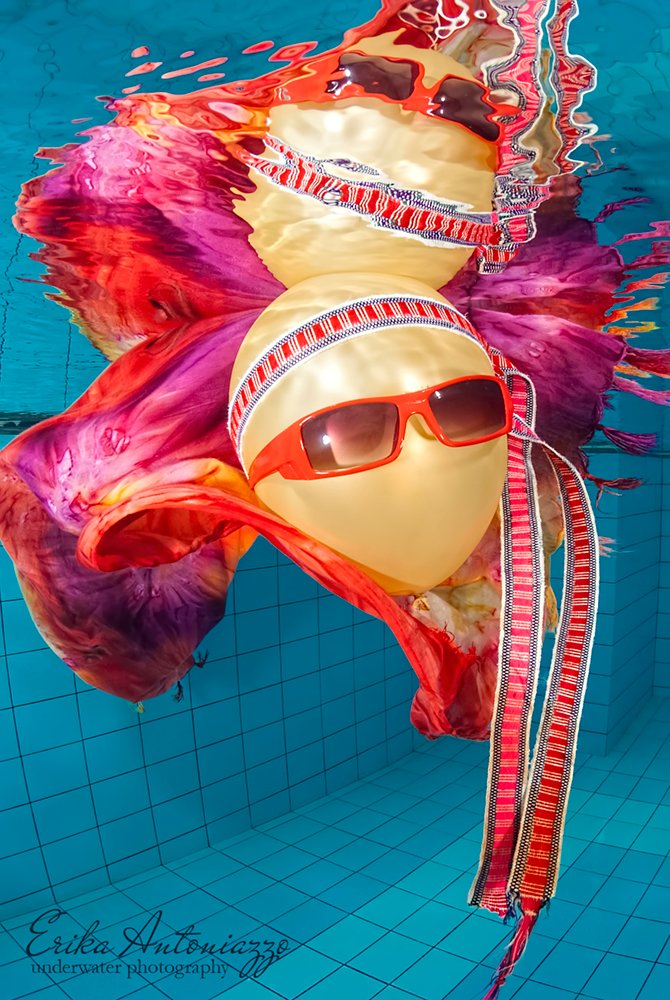Goudkleurige ballon met zonnebril, bandanna en oranje-rode doek onder water in het zwembad