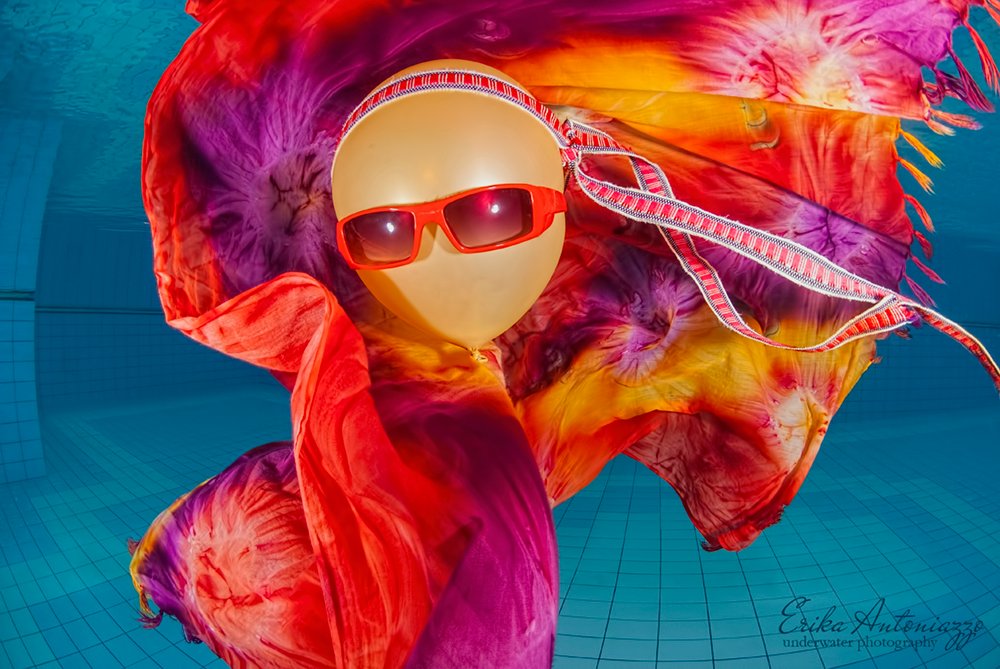 Goudkleurige ballon met zonnebril, bandanna en oranje-rode doek onder water in het zwembad