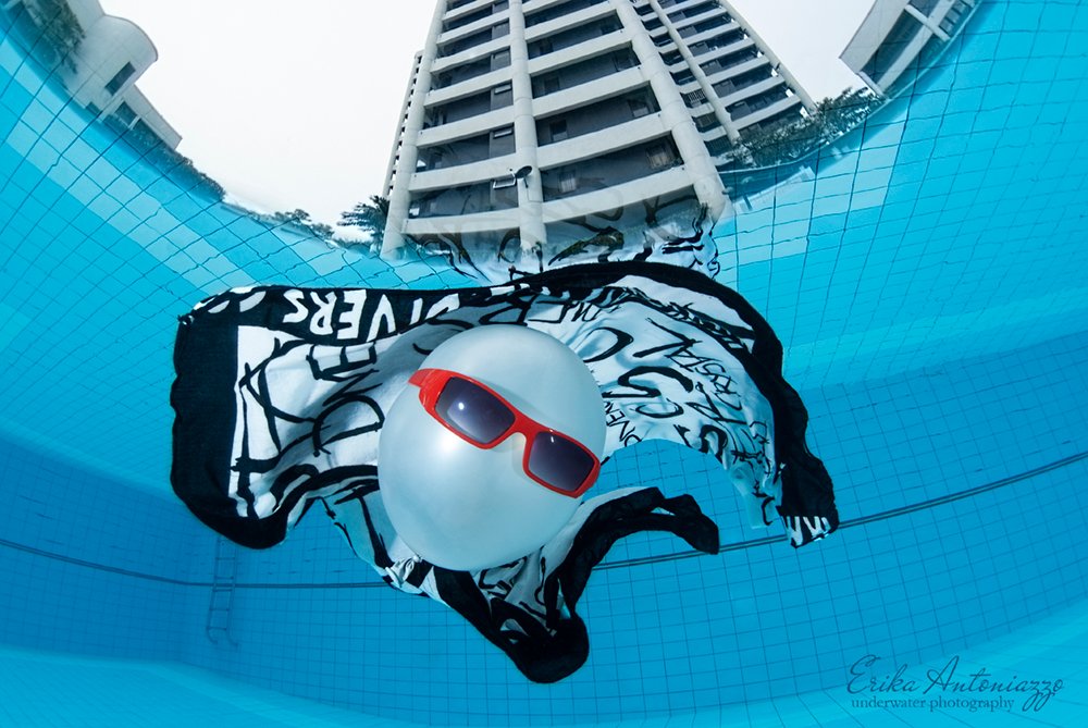 Witte ballon met zonnebril en zwart-witte doek onder water in het zwembad met een flatgebouw boven water
